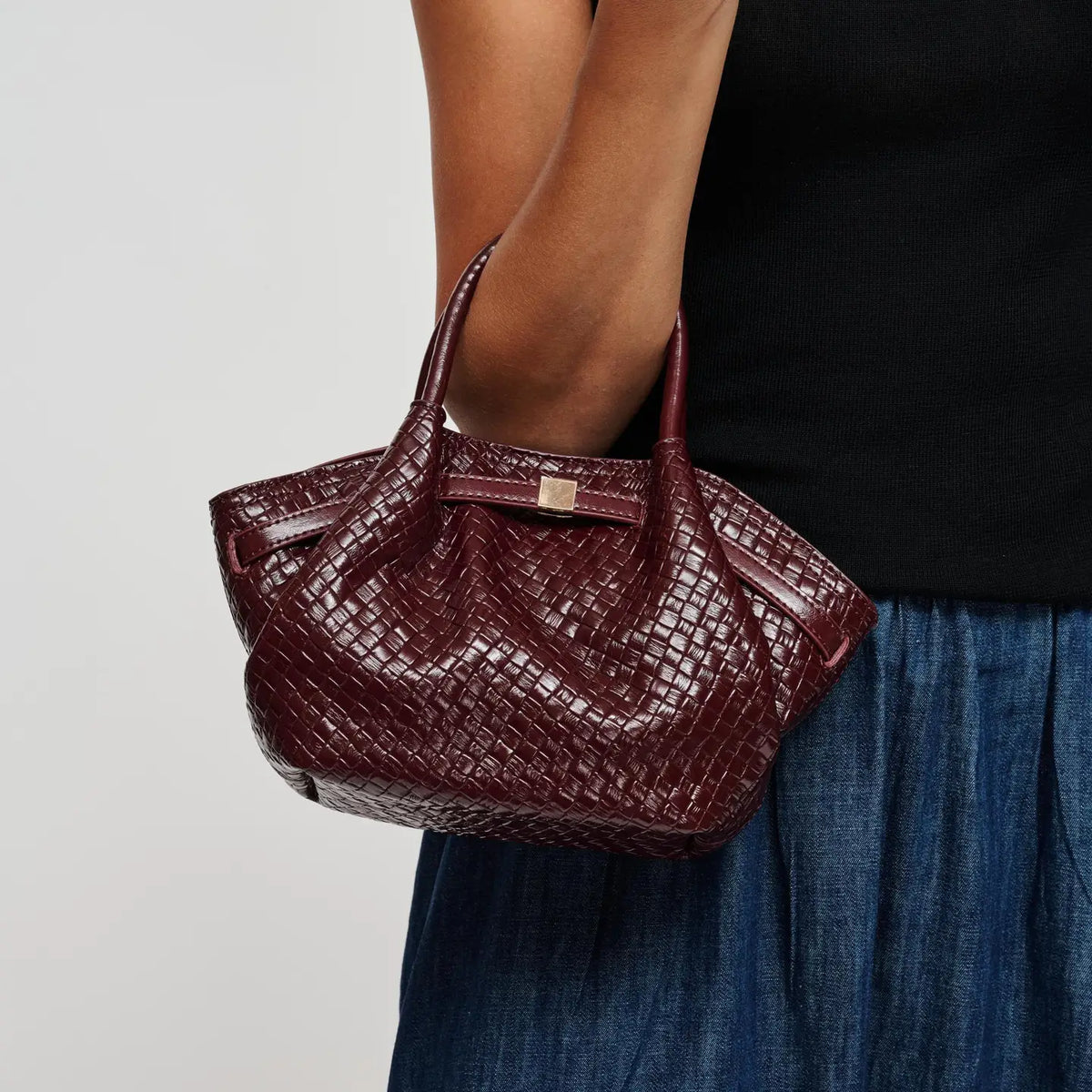 A sophisticated woven vegan leather crossbody featuring a textured embossed finish, sculpted side drape, and versatile top-handle and shoulder-strap styling.