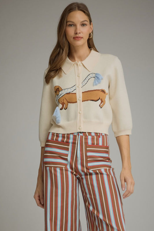 A playful knit cardigan featuring an adorable dachshund intarsia graphic, charming tassel details, and a classic button-front design.

