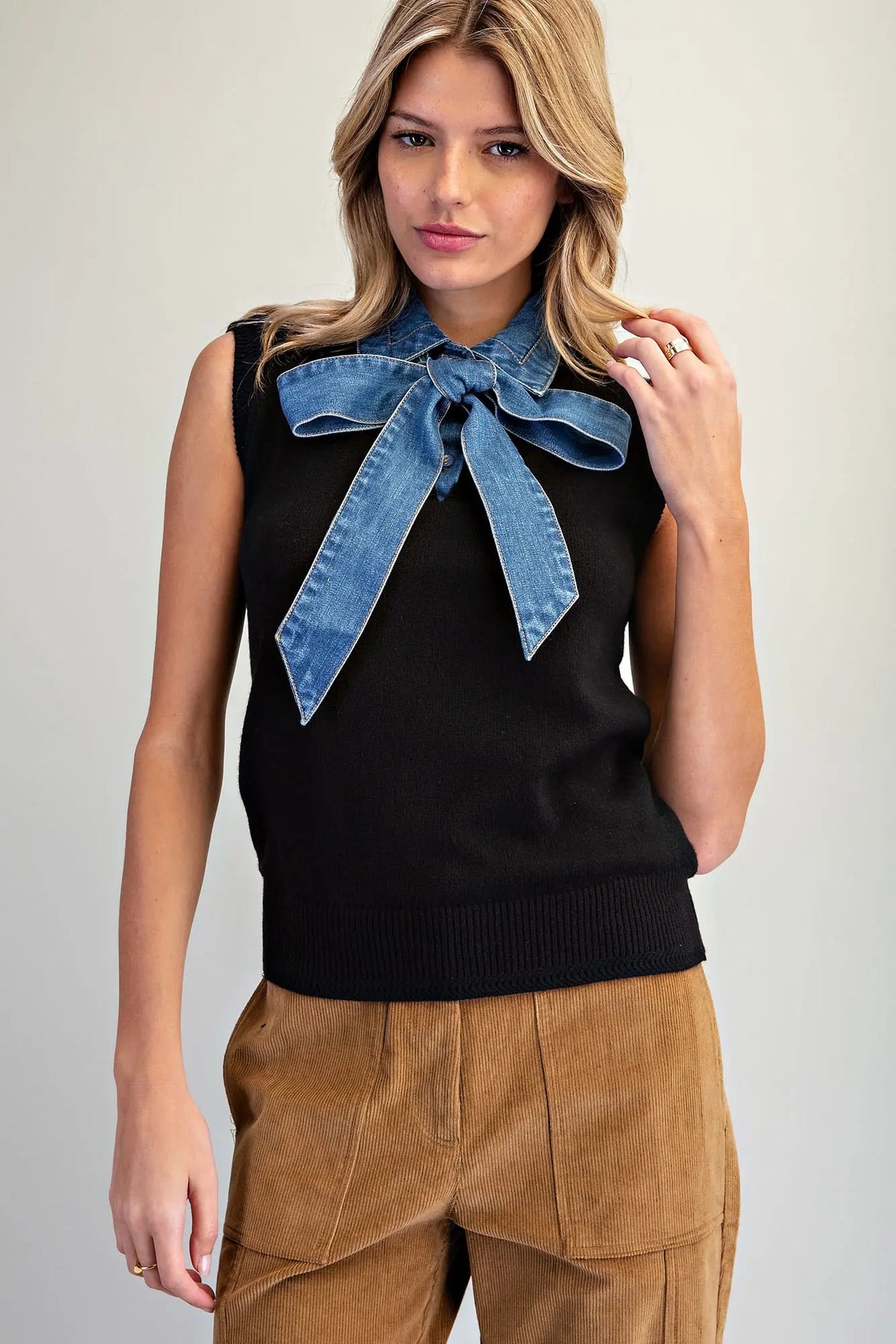 A stylish sleeveless knit top featuring a V-neckline, oversized denim tie-neck bow, and textured ribbed trim for a unique, polished look.