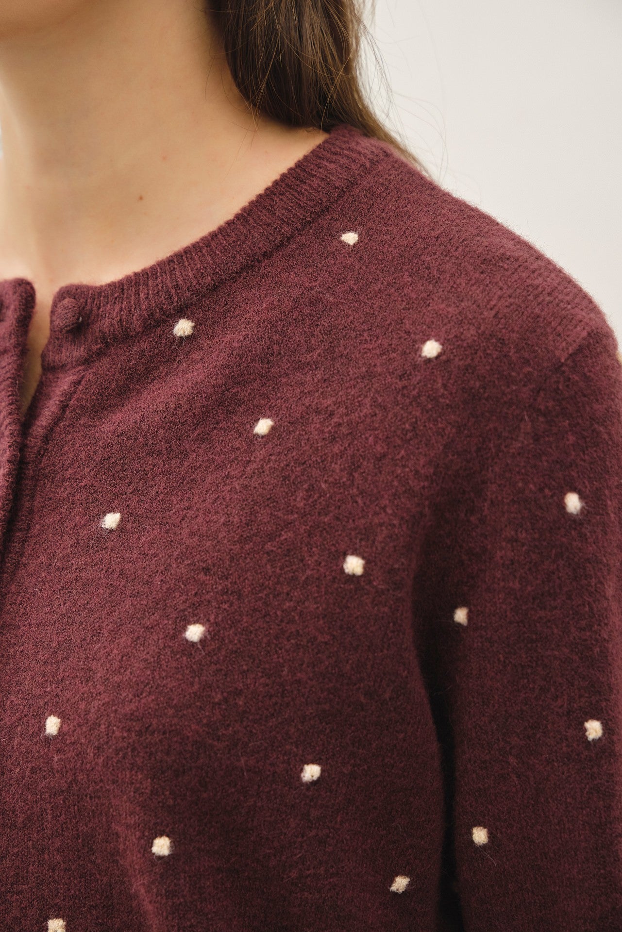 Close-up of burgundy knit sweater with small white embroidered dot details, showing the crewneck