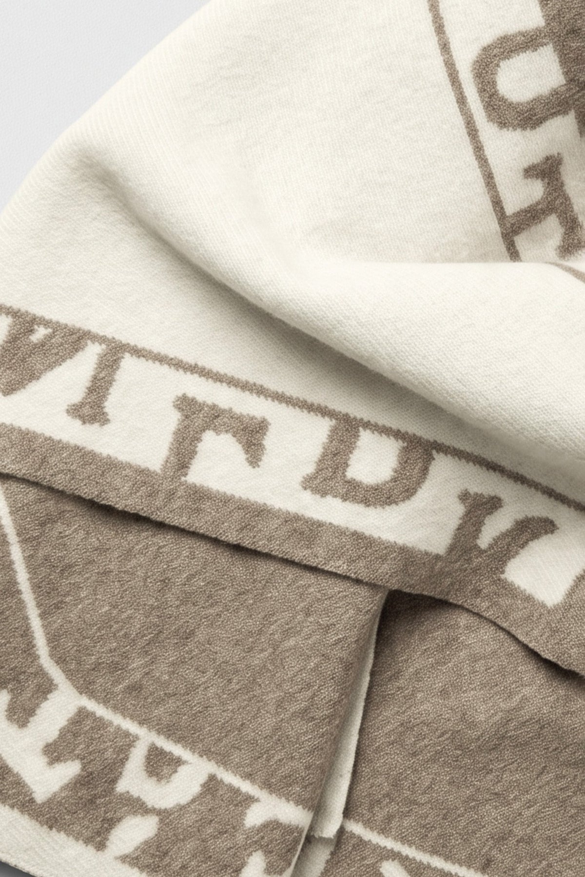 A cozy knit triangle scarf featuring reversible color blocking and stylish lettering details for a versatile cold-weather accessory.

