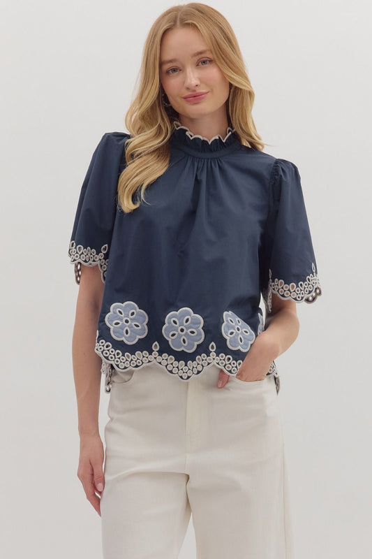 Romantic and airy, the Felicity top features floral embroidery, flutter sleeves, and a scalloped hem with a ruffled high neck.