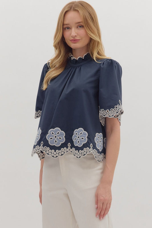 Romantic and airy, the Felicity top features floral embroidery, flutter sleeves, and a scalloped hem with a ruffled high neck.