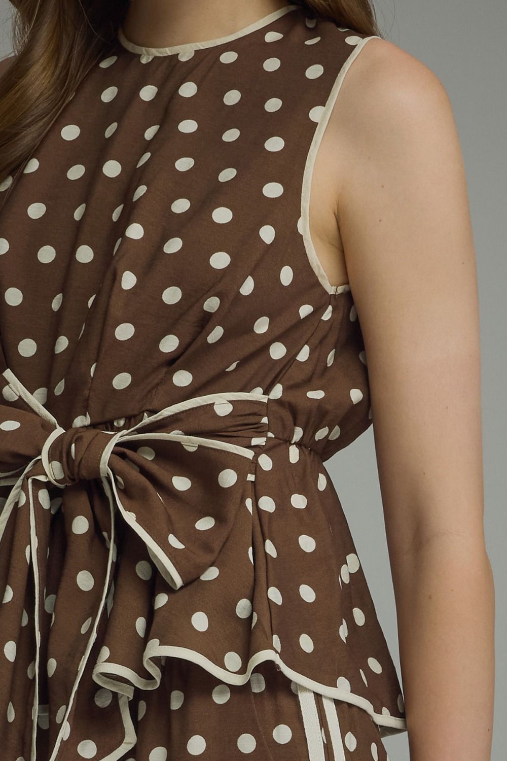 A timeless polka dot sleeveless top featuring a flattering tie waist and contrast trim for an effortlessly polished look.
