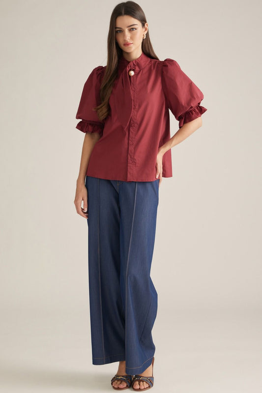 Women's solid woven blouse featuring a high neckline, front button closure, self-tie detail, short puff sleeves, ruffle trim, and elastic cuffs.