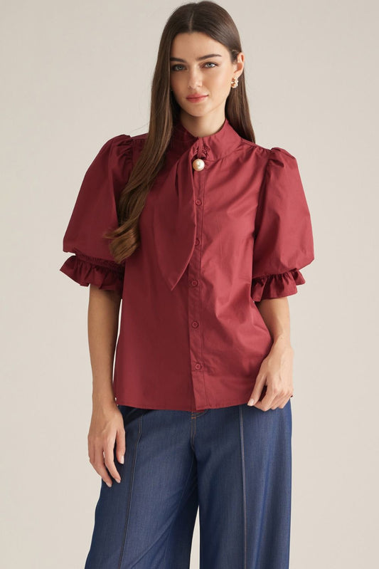 Women's solid woven blouse featuring a high neckline, front button closure, self-tie detail, short puff sleeves, ruffle trim, and elastic cuffs.