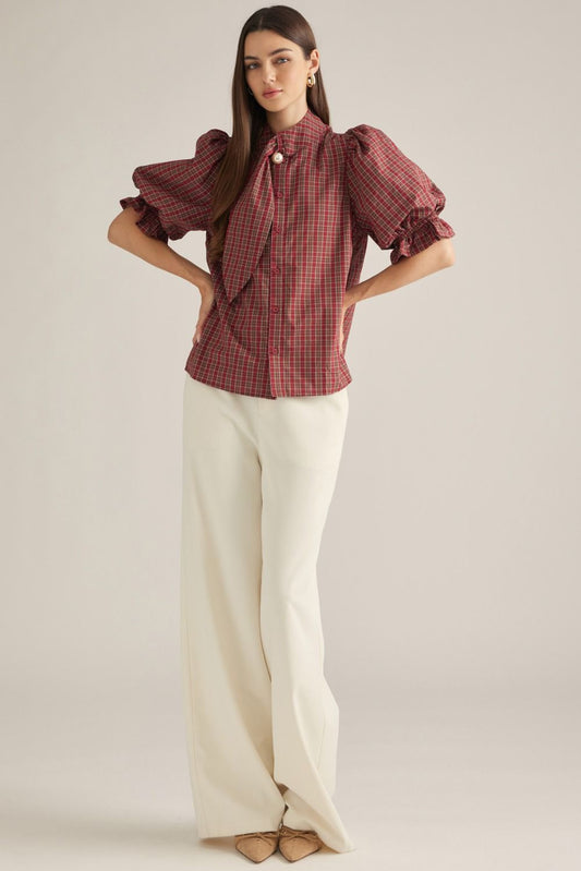 Women's plaid top with short puff sleeves, high neckline, necktie detail, pearl accent, and ruffle trim