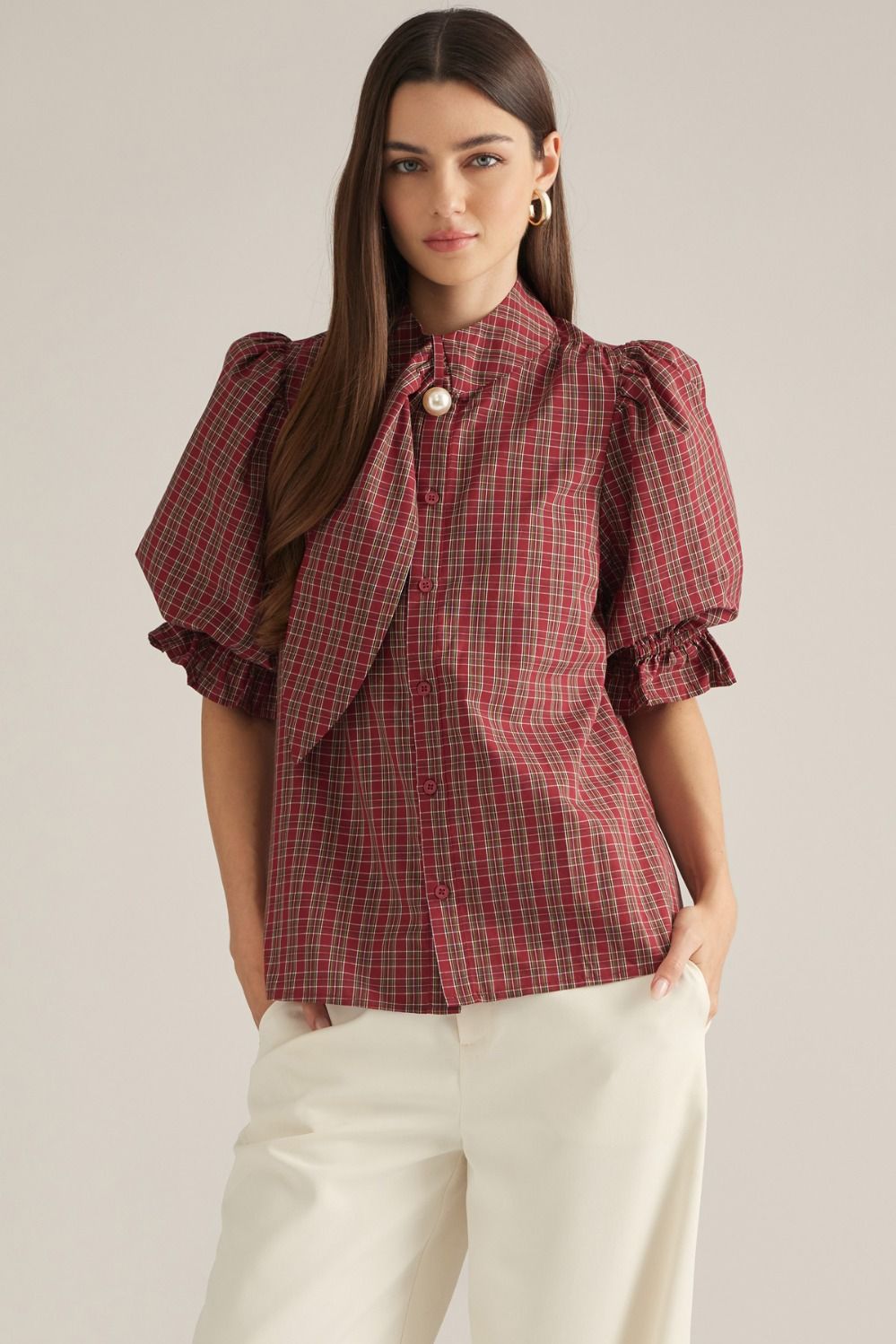 Women's plaid top with short puff sleeves, high neckline, necktie detail, pearl accent, and ruffle trim