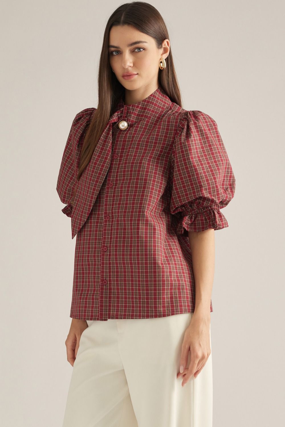 Women's plaid top with short puff sleeves, high neckline, necktie detail, pearl accent, and ruffle trim