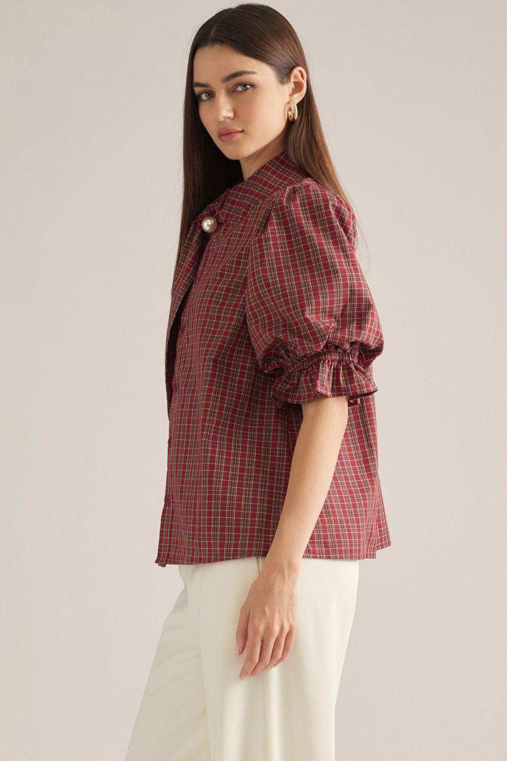 Women's plaid top with short puff sleeves, high neckline, necktie detail, pearl accent, and ruffle trim