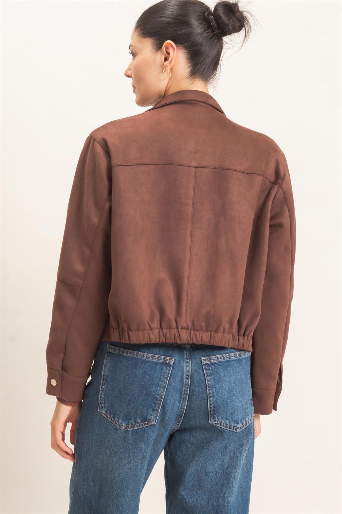 A polished faux suede jacket featuring a structured silhouette, high collar, metal snap closures, subtle stitching, and convenient side pockets.