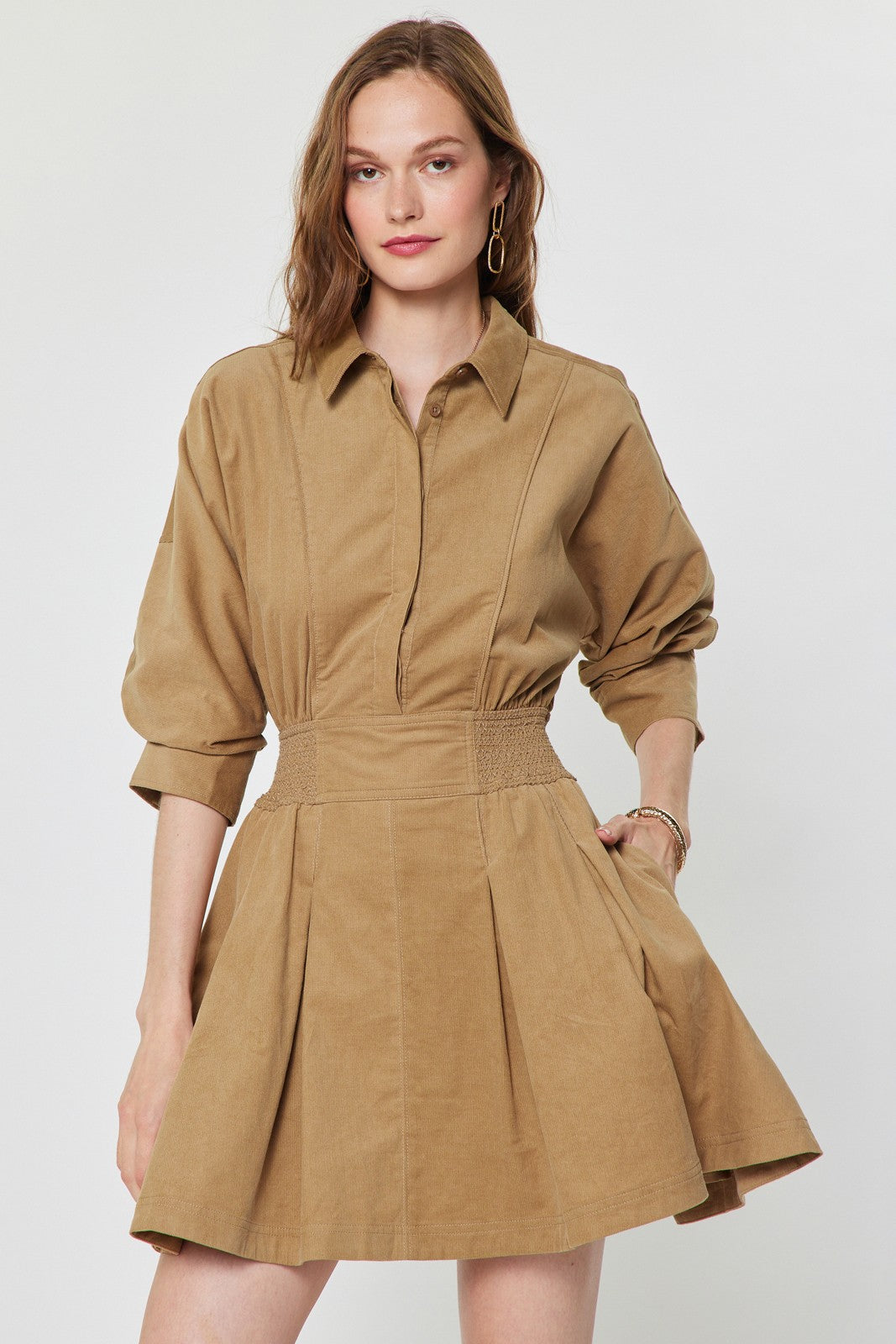 A charming cotton corduroy mini dress featuring a classic shirt collar, smocked waist, flattering A-line skirt, and practical side pockets.