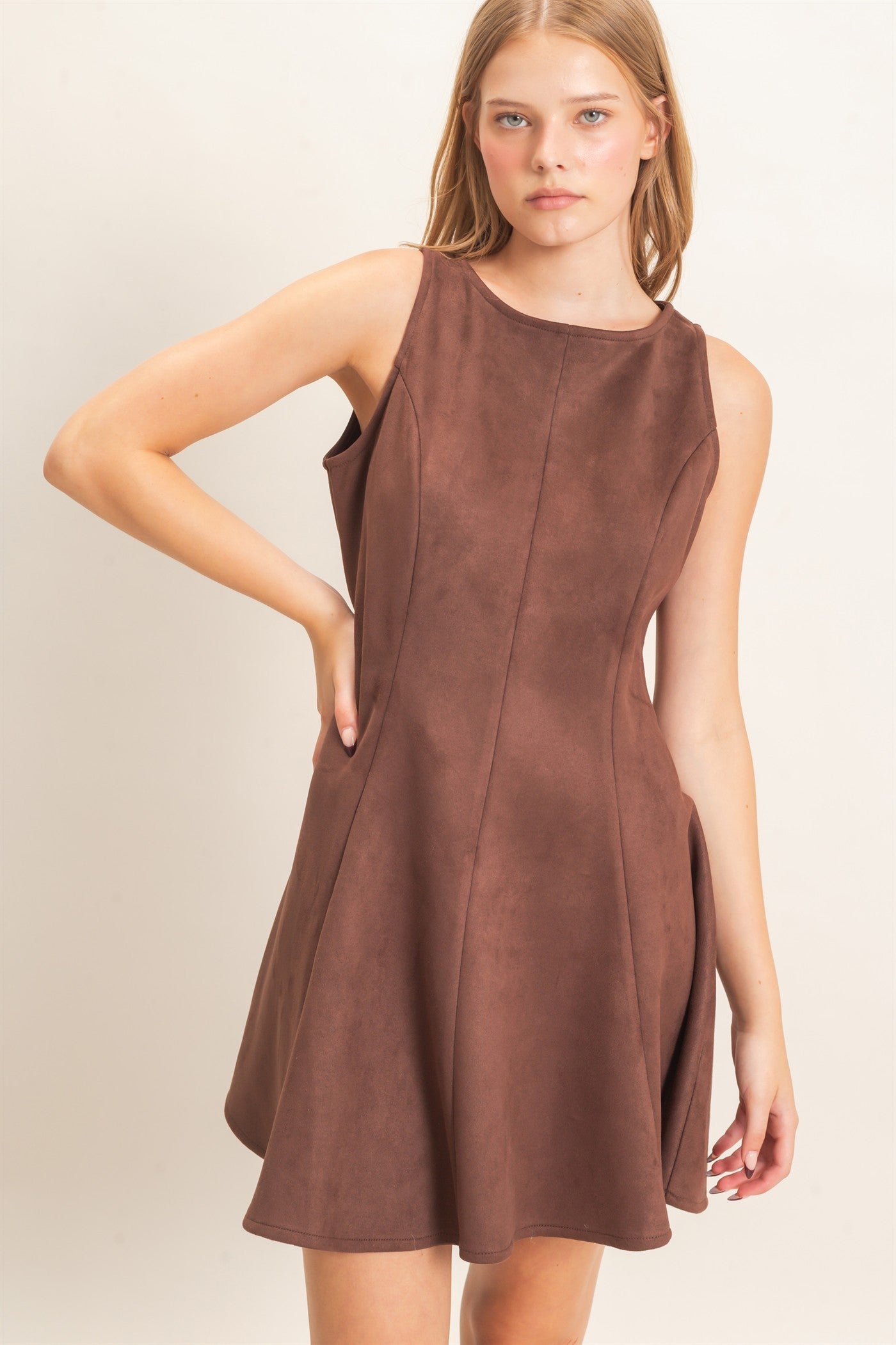 A sophisticated sleeveless suede mini dress with a classic round neckline and flattering flared silhouette that effortlessly transitions from day to night.
