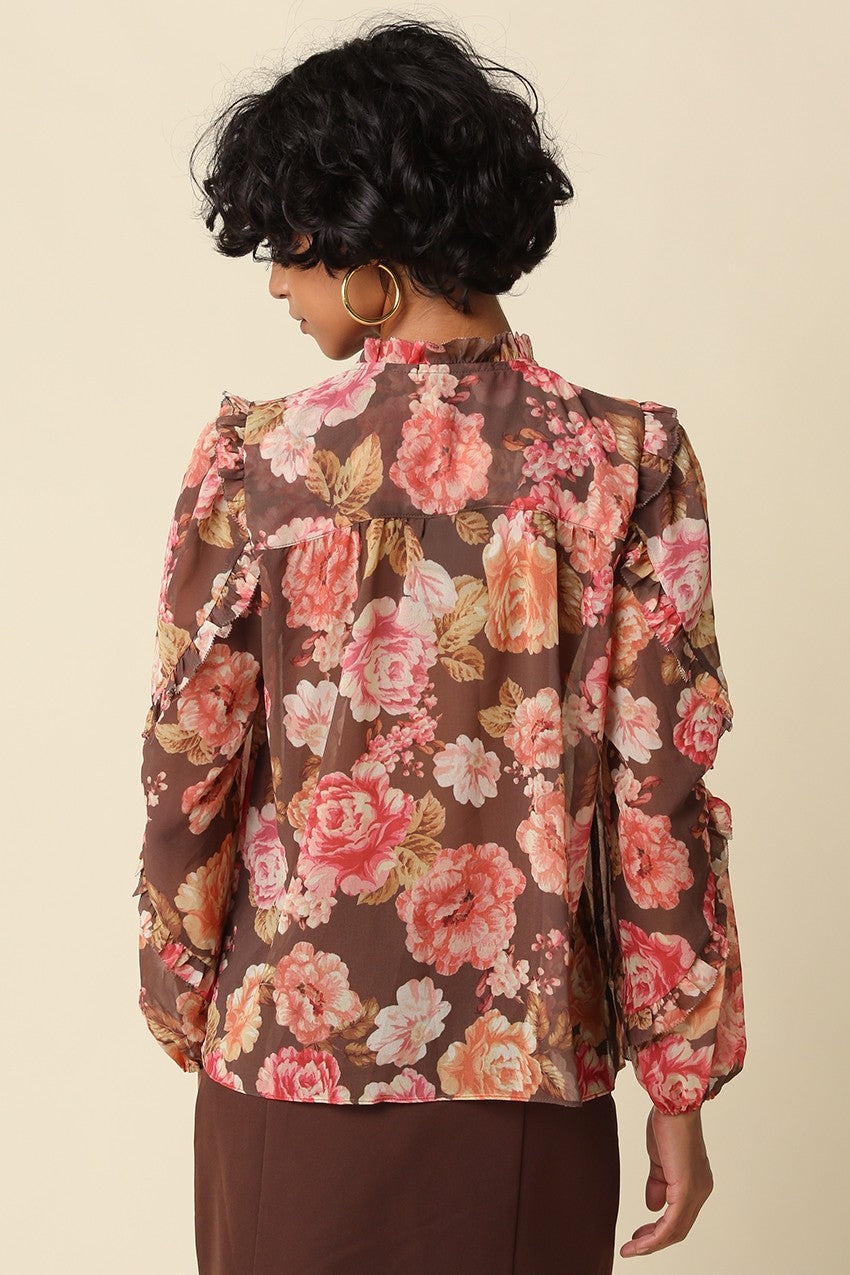 A romantic floral blouse featuring a ruffle mock neckline, elegant self-tie detail, long puff sleeves, and tiered ruffle cuffs.

