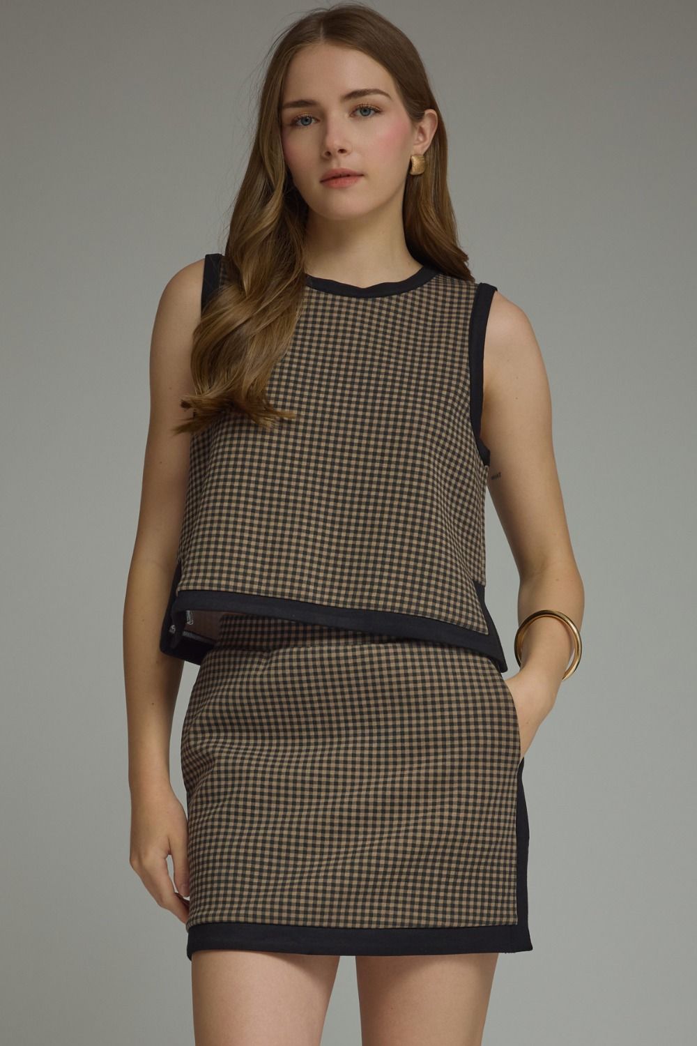 A charming gingham knit top featuring contrast binding, a layered hem, and a lightweight sleeveless silhouette perfect for effortless everyday style.