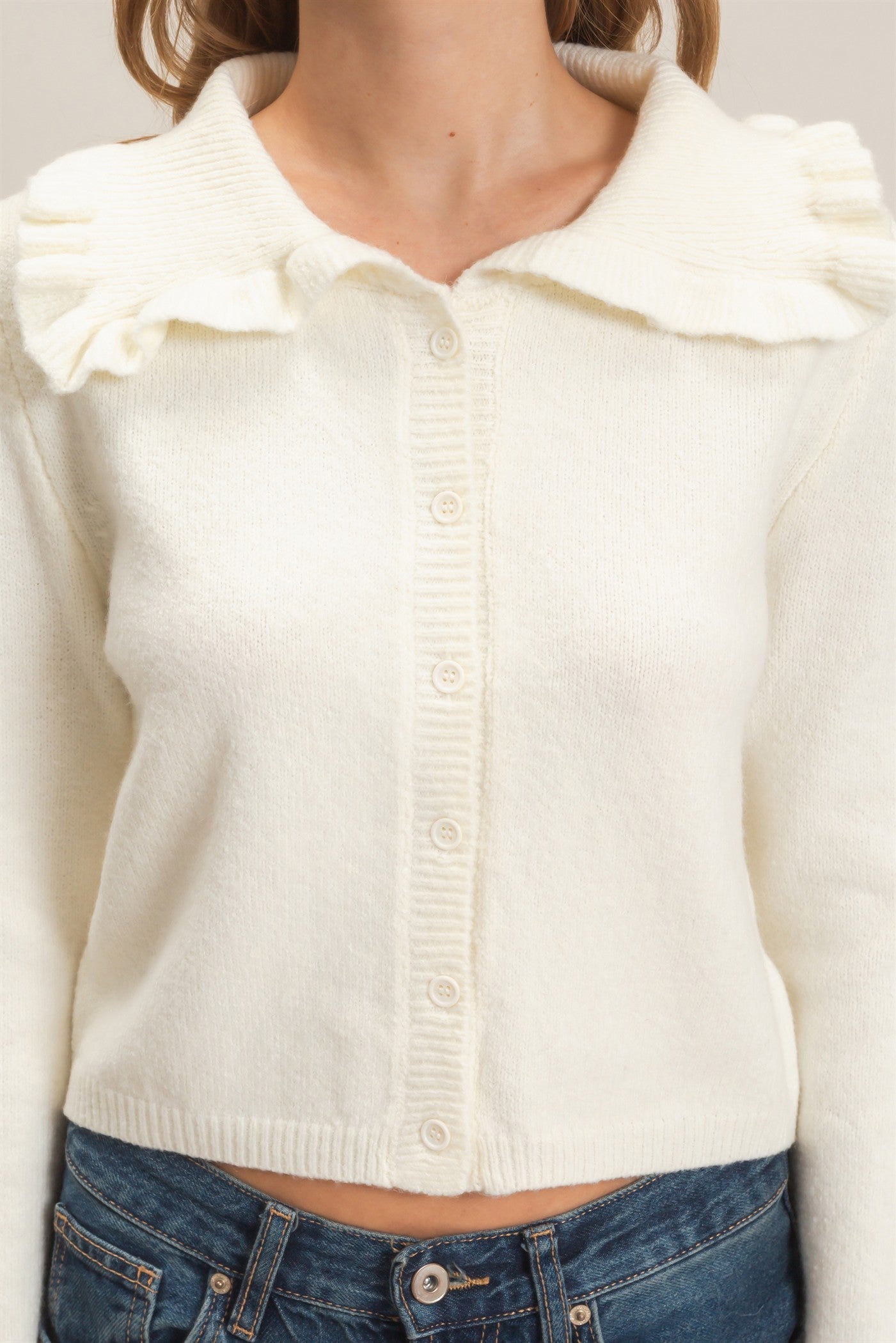 A polished knit cardigan featuring a feminine ruffled collar, classic button-front design, and ribbed cuffs for timeless everyday elegance.
