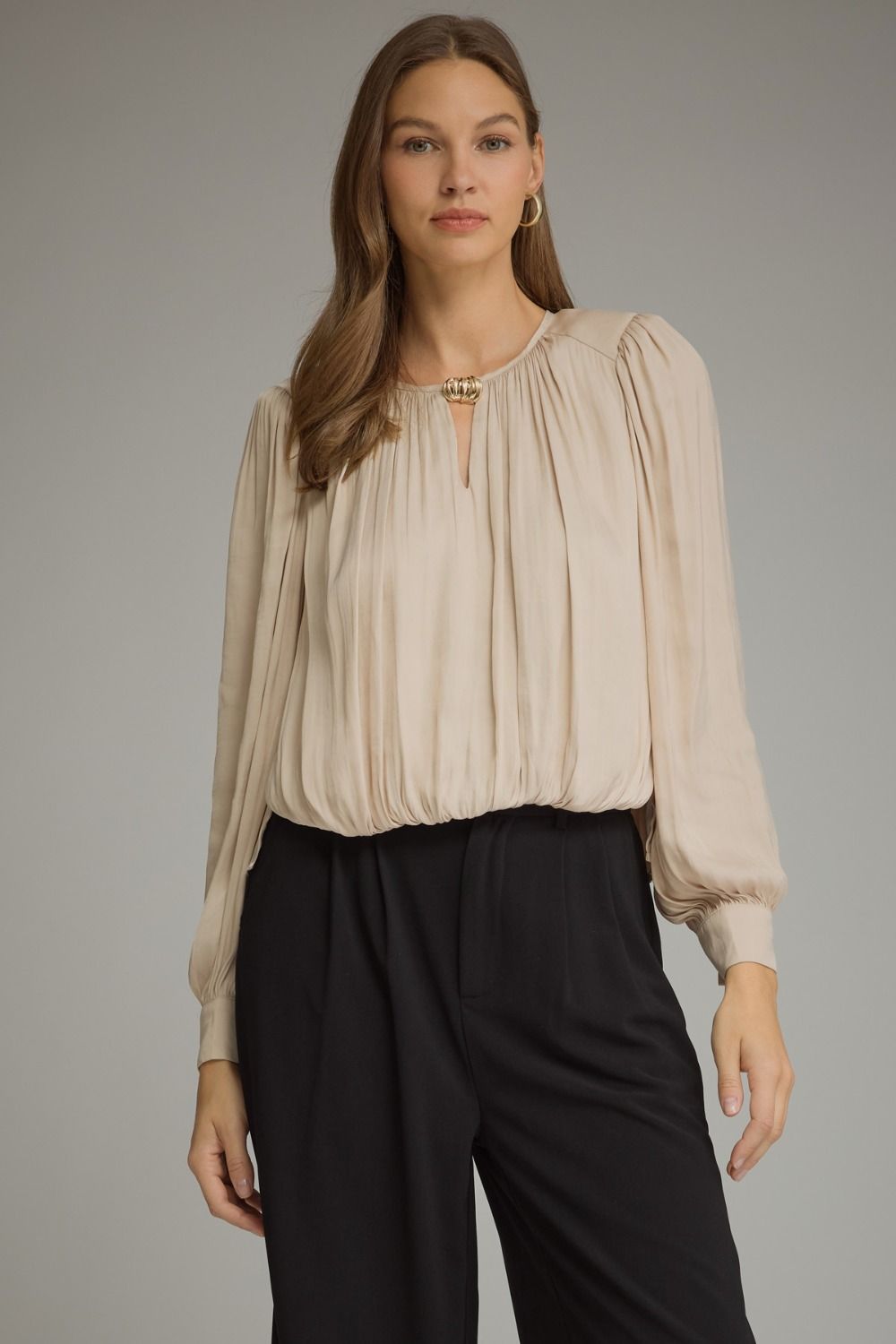 A polished long sleeve top featuring elegant keyhole details, gathered texture, and refined gold hardware at the neckline.

