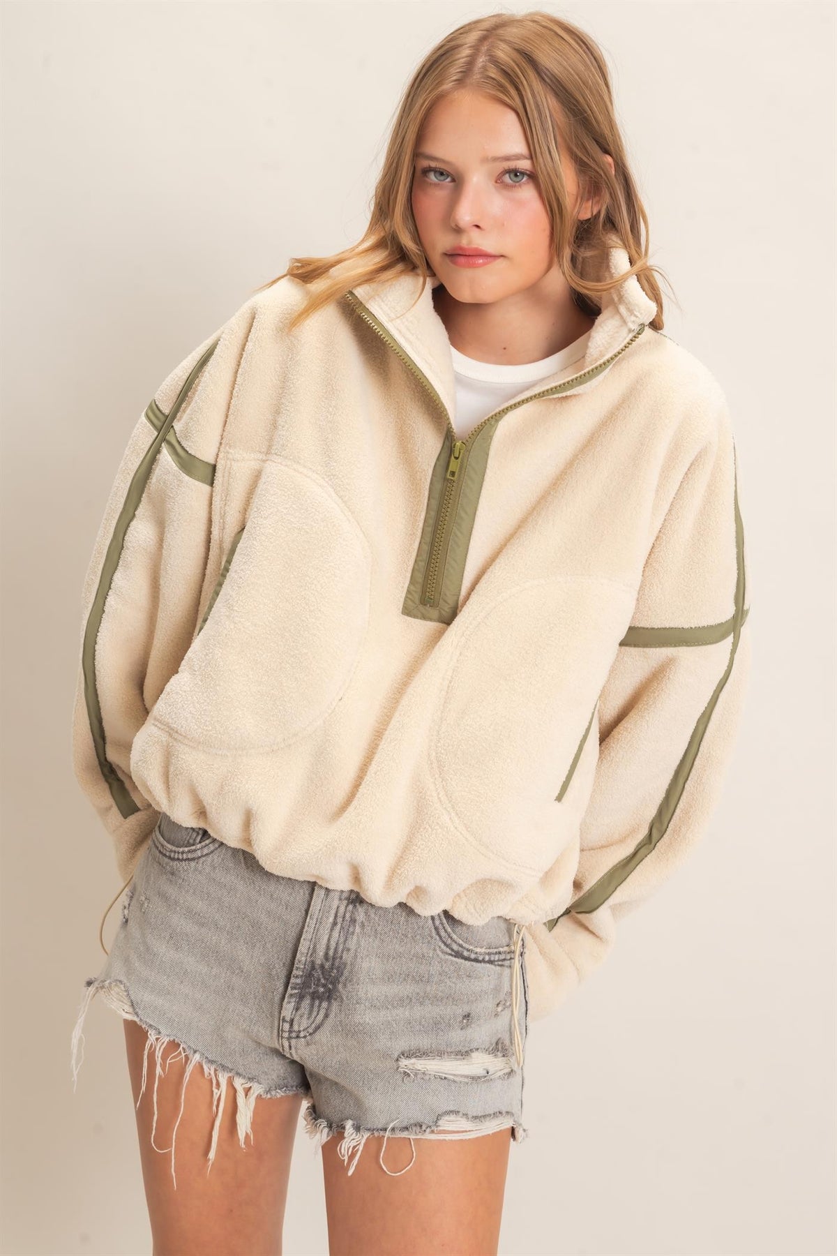 A cozy fleece half zip pullover featuring a high funnel neck, sporty contrast trim, oversized curved pockets, and an adjustable drawstring hem.