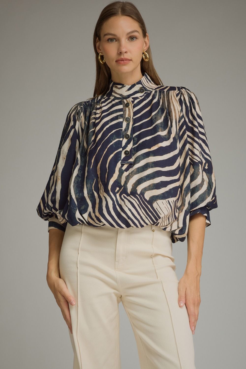 A statement-making zebra print top featuring elegant ¾ balloon sleeves, a stand collar, gathered details, and a polished banded hem.

