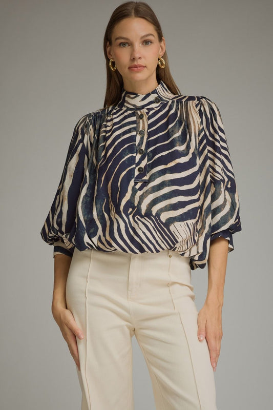 A statement-making zebra print top featuring elegant ¾ balloon sleeves, a stand collar, gathered details, and a polished banded hem.

