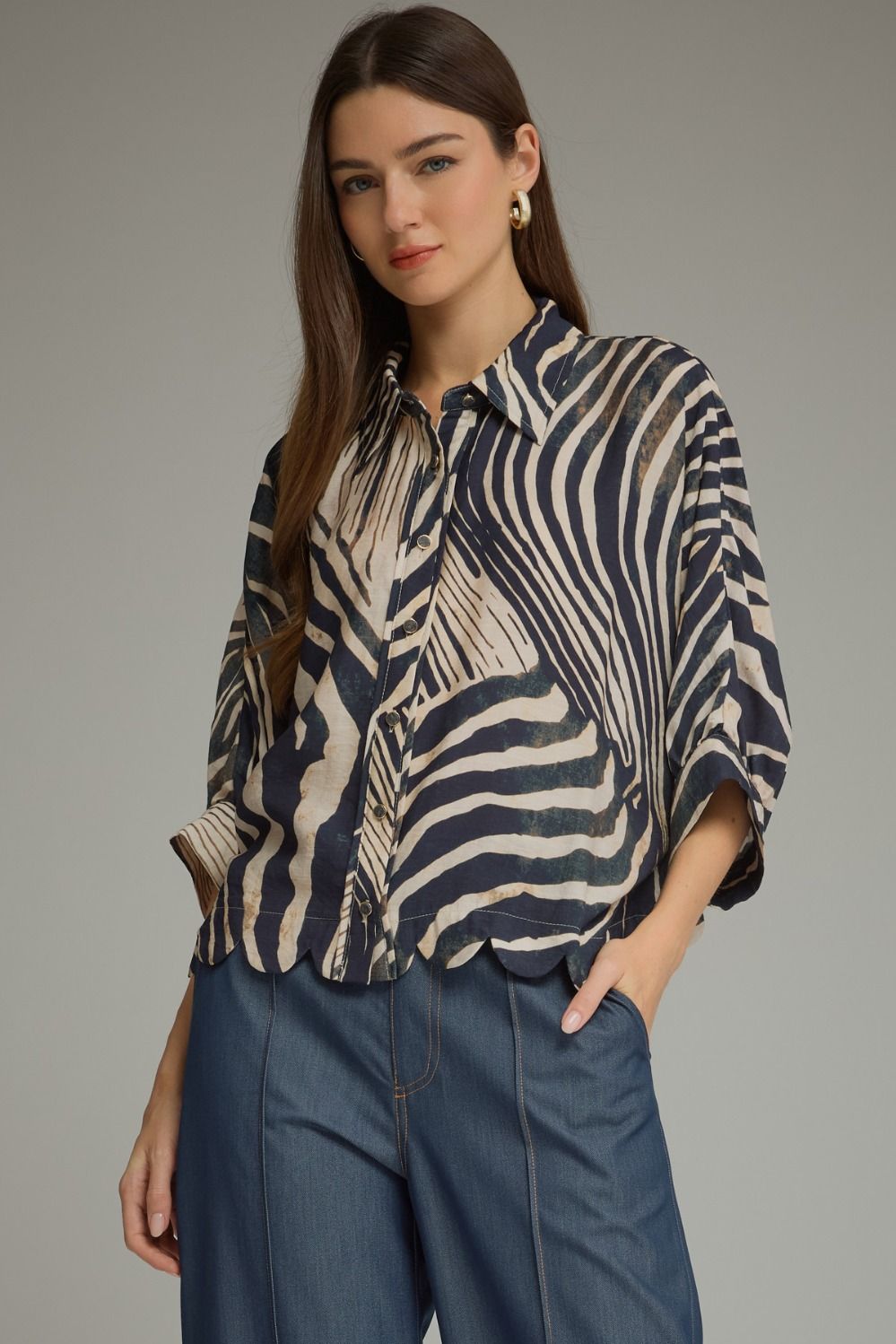 A chic zebra-print woven top featuring dramatic poncho sleeves, a classic shirt collar, button-front closure, and a feminine scalloped hem.