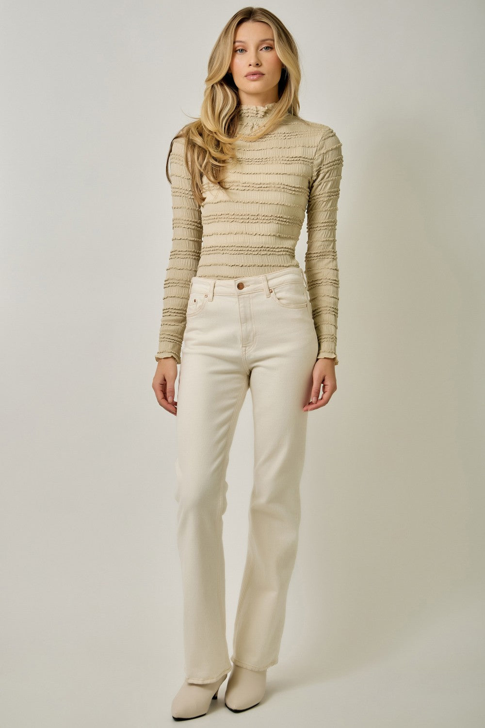 A feminine fitted knit top featuring a sleek mock neckline, long sleeves, and playful ruffled lettuce-edge stripes for a flattering statement look.
