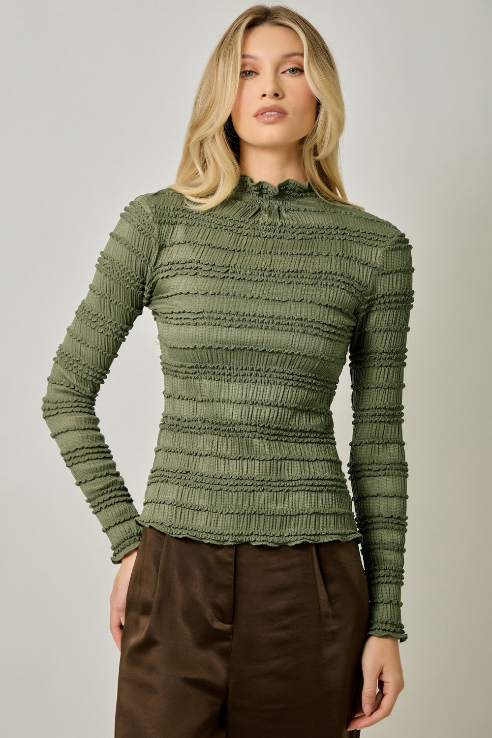 A feminine fitted knit top featuring a sleek mock neckline, long sleeves, and playful ruffled lettuce-edge stripes for a flattering statement look.
