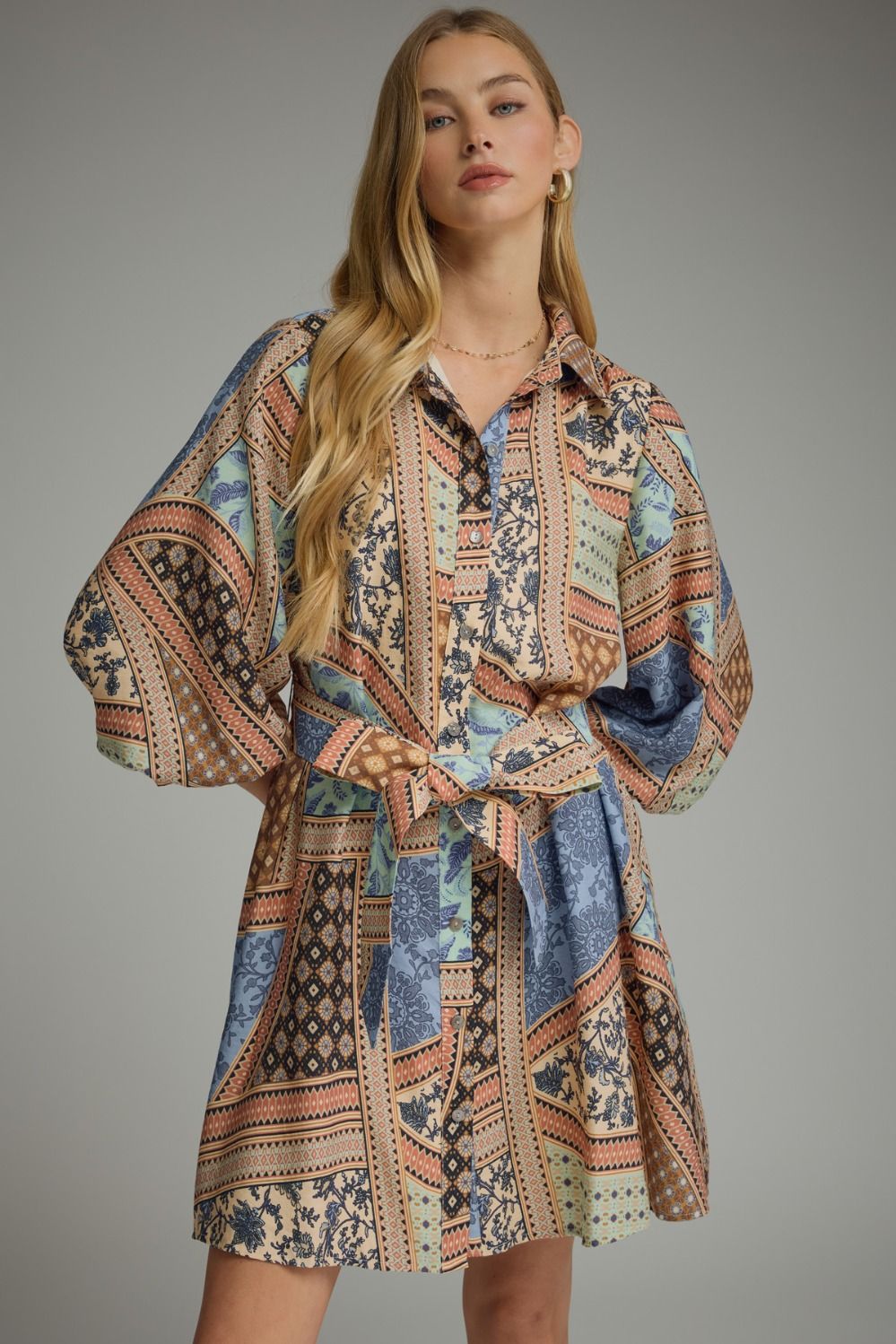A charming patchwork print mini dress featuring ¾ sleeves, a button-front closure, self-tie waist, and convenient side pockets for effortless everyday style.