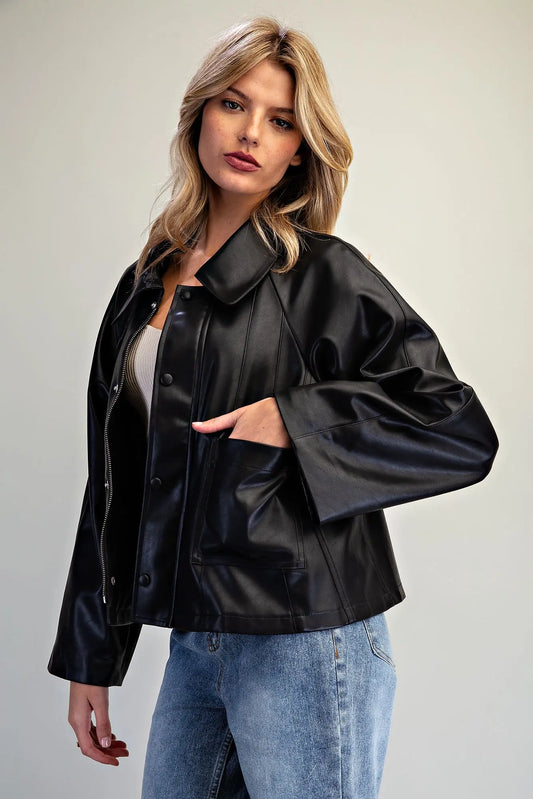 A fashion-forward pleather jacket featuring a flared boxy silhouette, dramatic wide raglan sleeves, paneled seams, and a sleek hidden zip-and-snap front.
