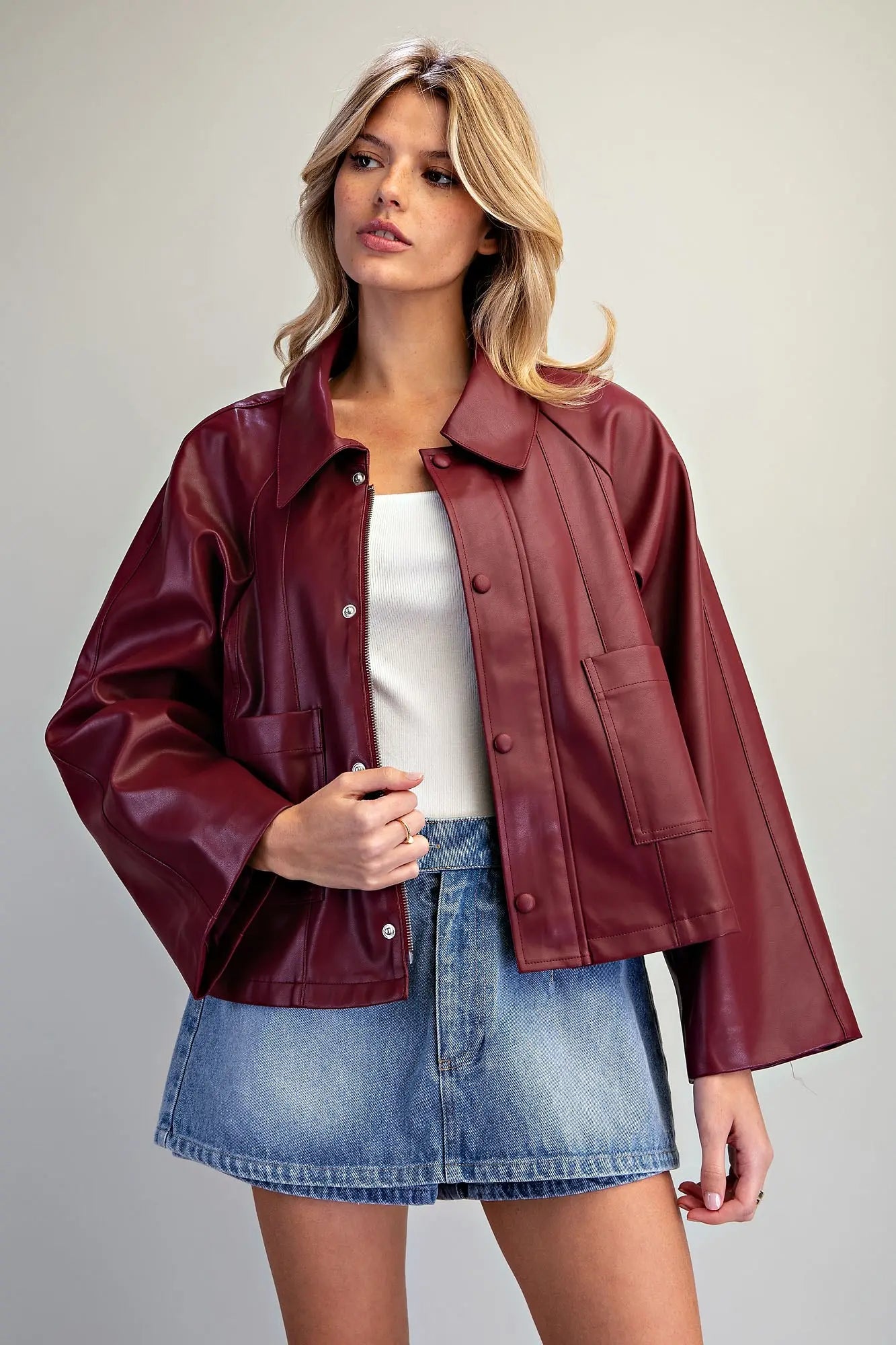 A fashion-forward pleather jacket featuring a flared boxy silhouette, dramatic wide raglan sleeves, paneled seams, and a sleek hidden zip-and-snap front.
