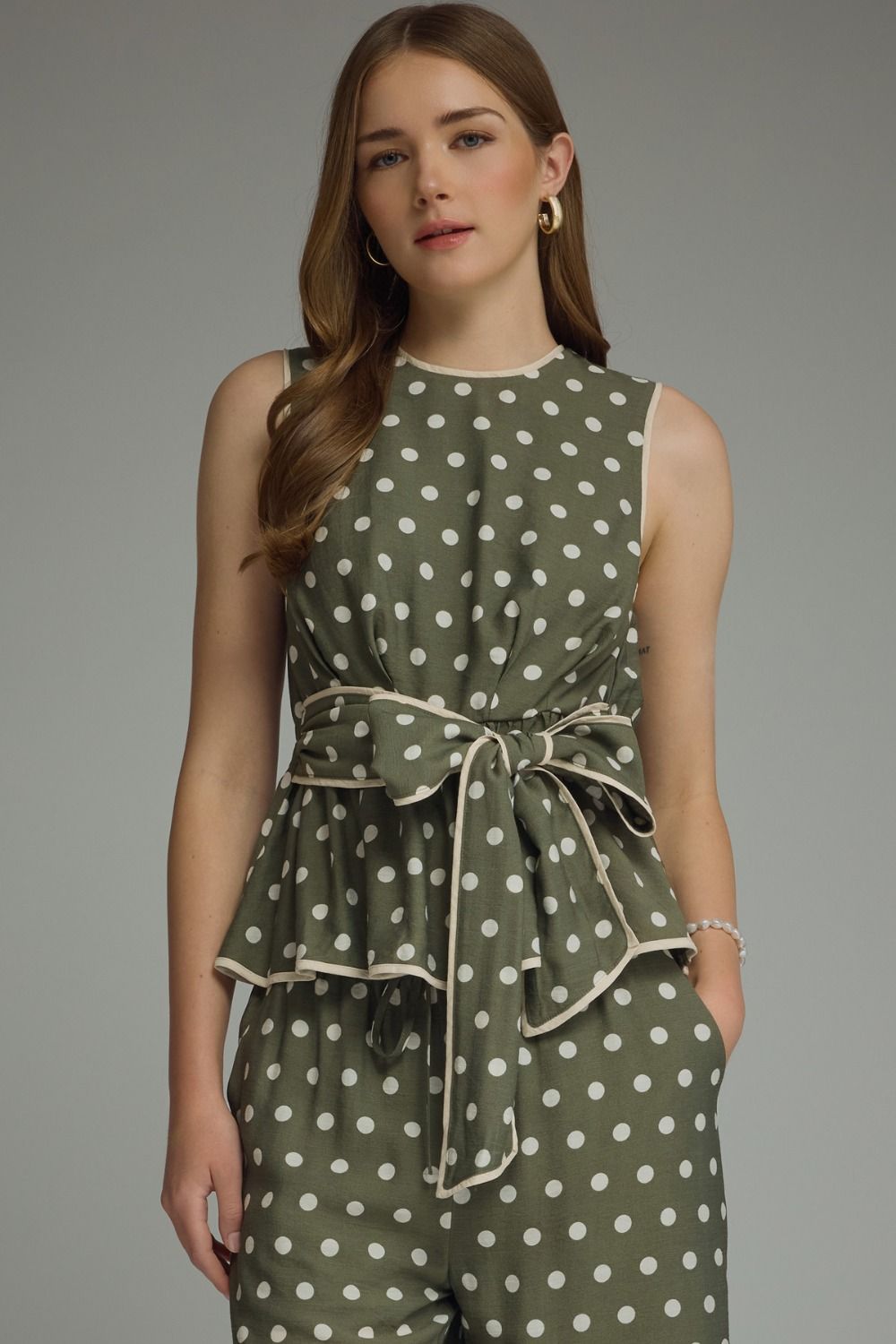 A timeless polka dot sleeveless top featuring a flattering tie waist and contrast trim for an effortlessly polished look.
