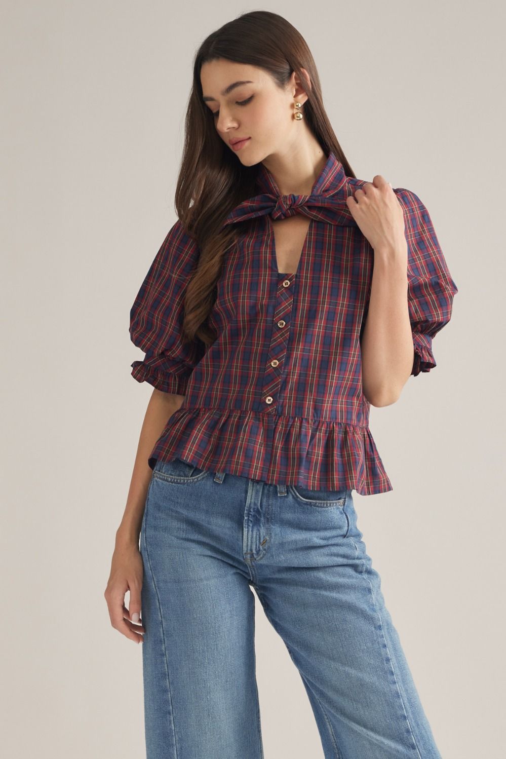 A charming plaid top featuring romantic puff sleeves, a coordinating scarf detail, ruffle hem, and classic button-front styling.