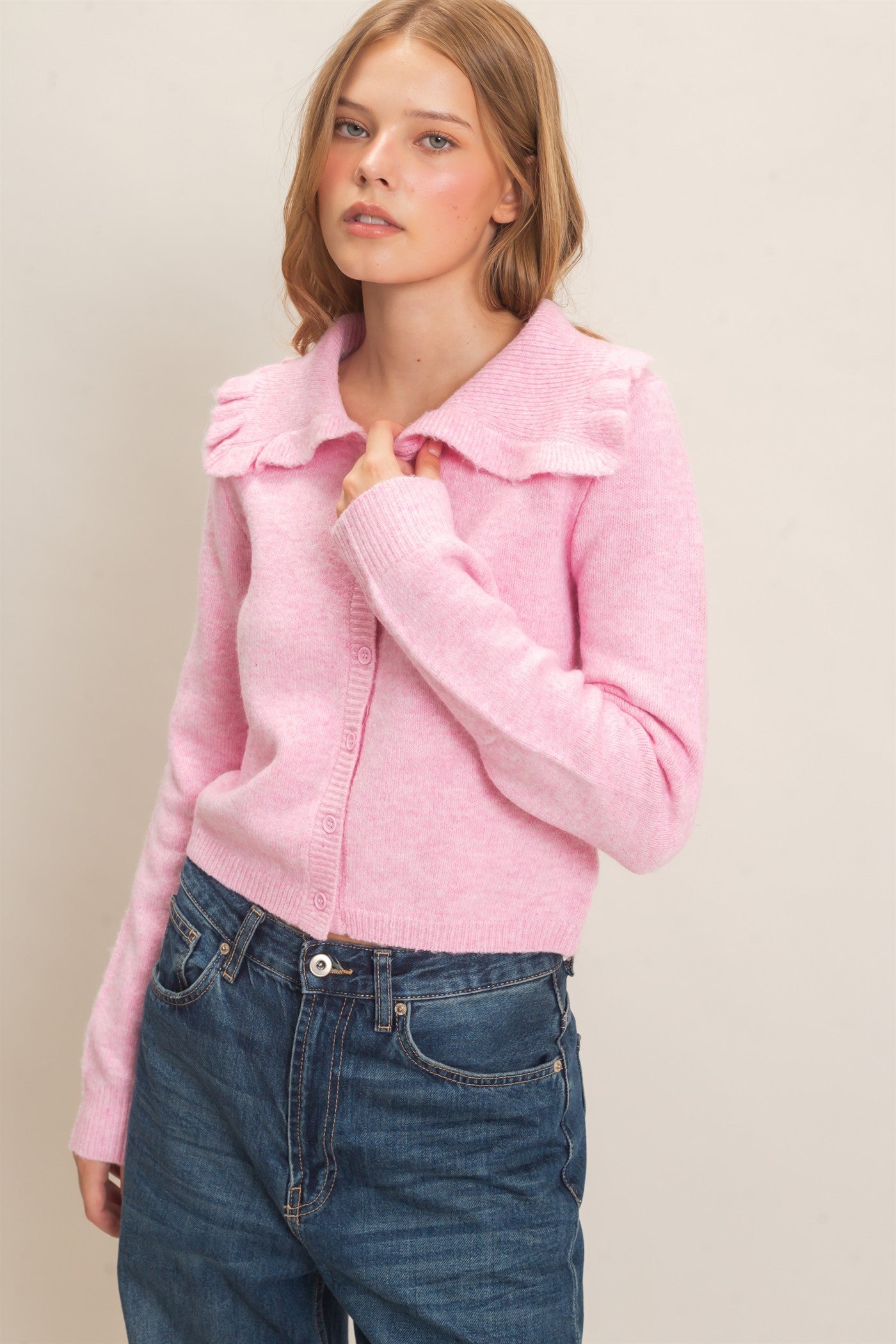 A polished knit cardigan featuring a feminine ruffled collar, classic button-front design, and ribbed cuffs for timeless everyday elegance.
