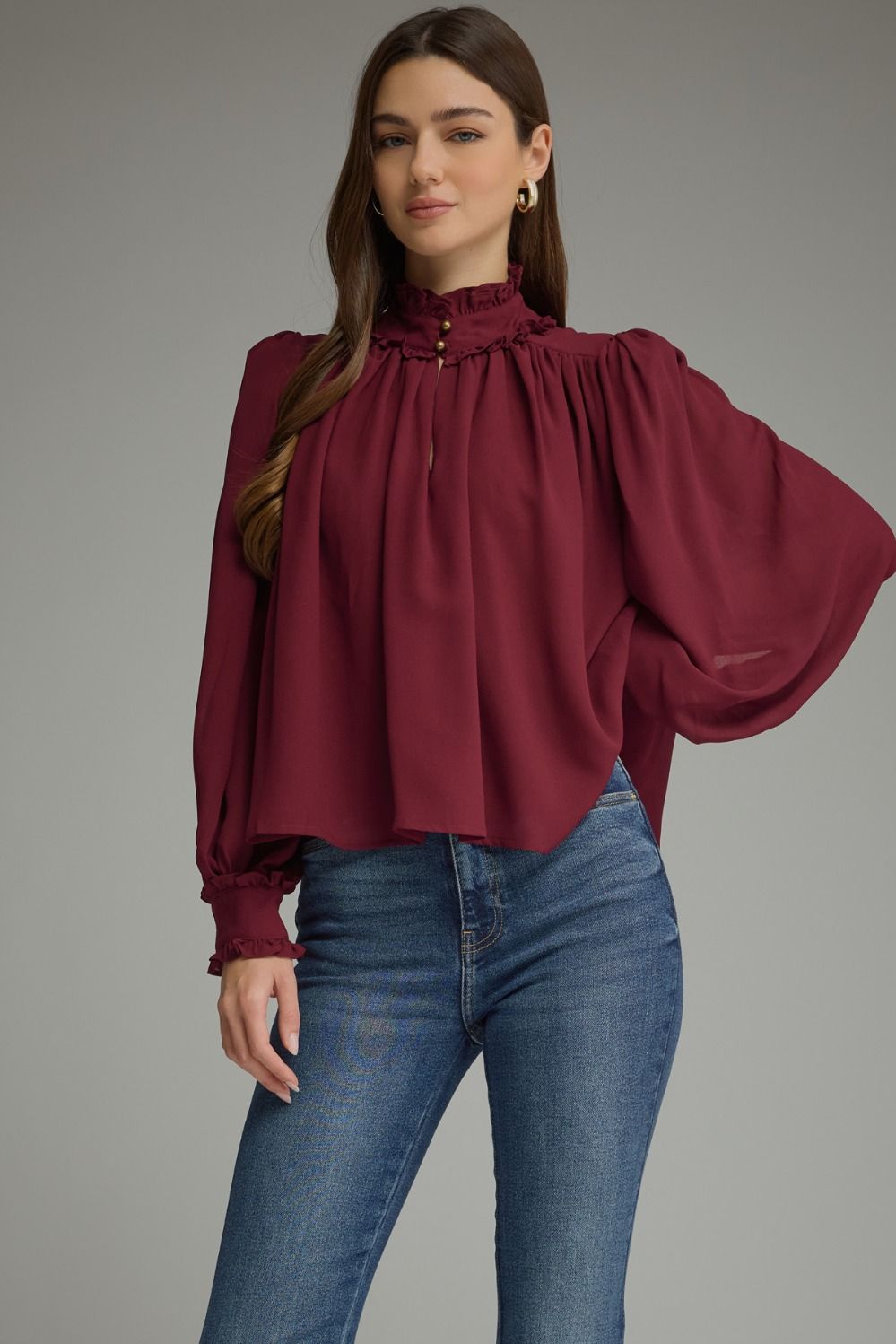 A romantic long sleeve blouse featuring a ruffled high neckline, gathered details, voluminous sleeves, and delicate ruffle-trimmed cuffs.

