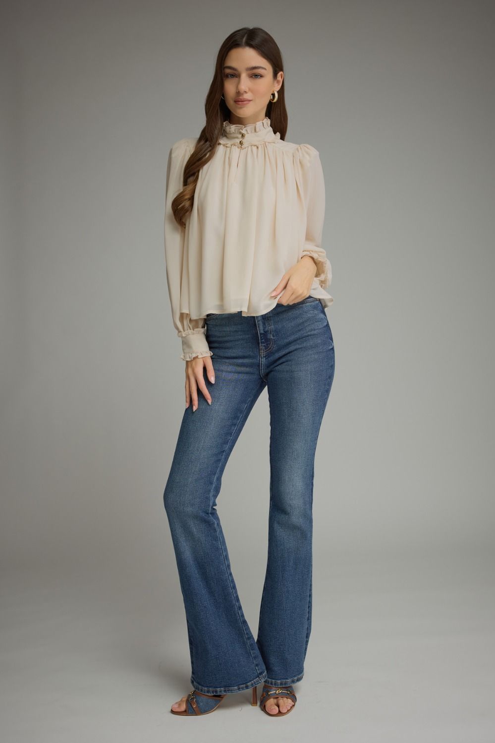 A romantic long sleeve blouse featuring a ruffled high neckline, gathered details, voluminous sleeves, and delicate ruffle-trimmed cuffs.

