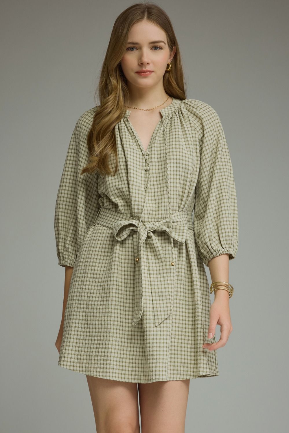 A timeless gingham mini dress featuring ¾ sleeves, a self-tie waist belt, and a button-front design for effortlessly polished style.
