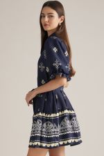 A charming printed mini dress featuring puff sleeves, a classic shirt collar, self-tie waist, and playful ruffle hem finished with a contrasting border print.