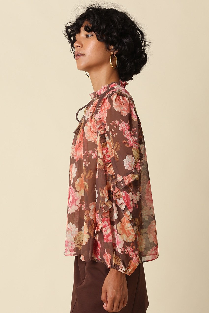 A romantic floral blouse featuring a ruffle mock neckline, elegant self-tie detail, long puff sleeves, and tiered ruffle cuffs.

