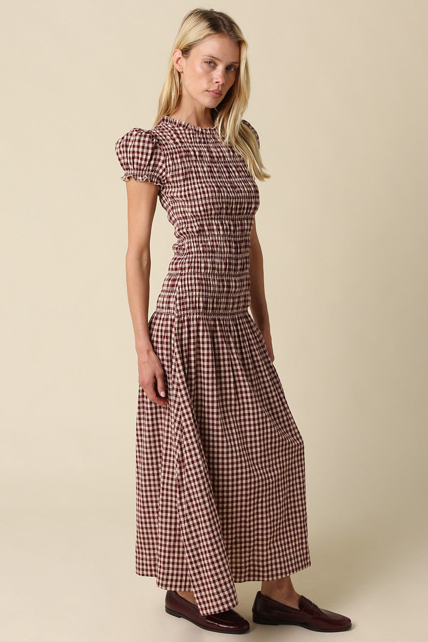 A romantic plaid maxi dress featuring soft puff sleeves, a fitted smocked bodice, and a flowing gathered skirt for an effortlessly feminine silhouette.