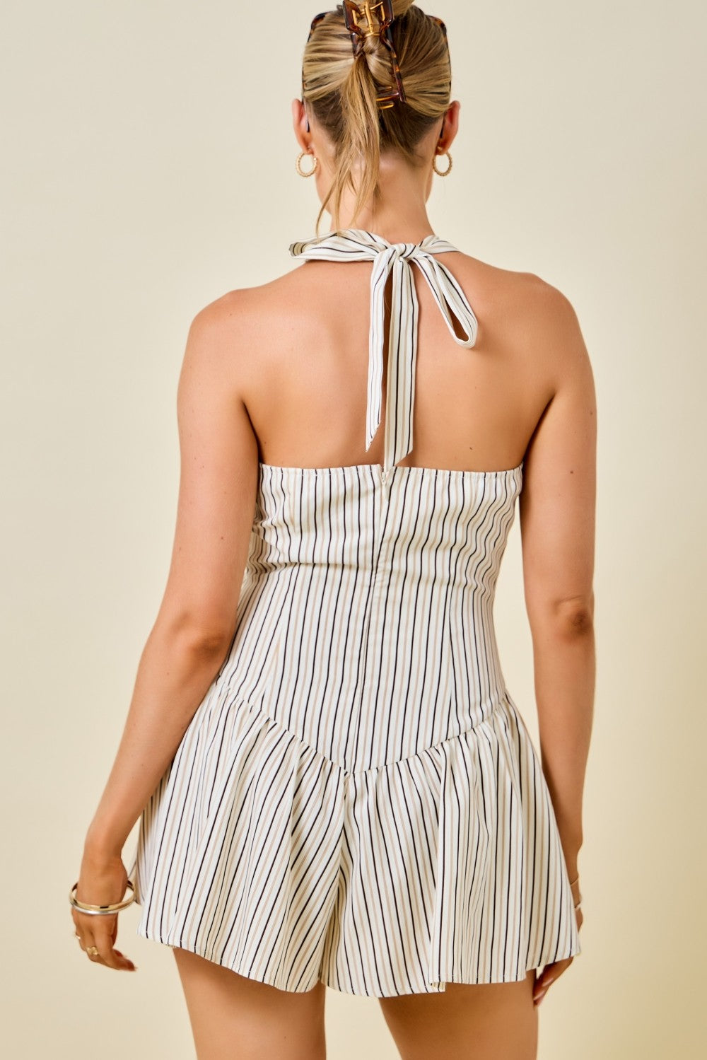 sleeveless halter-neck romper with vertical brown pinstripes on a cream background.