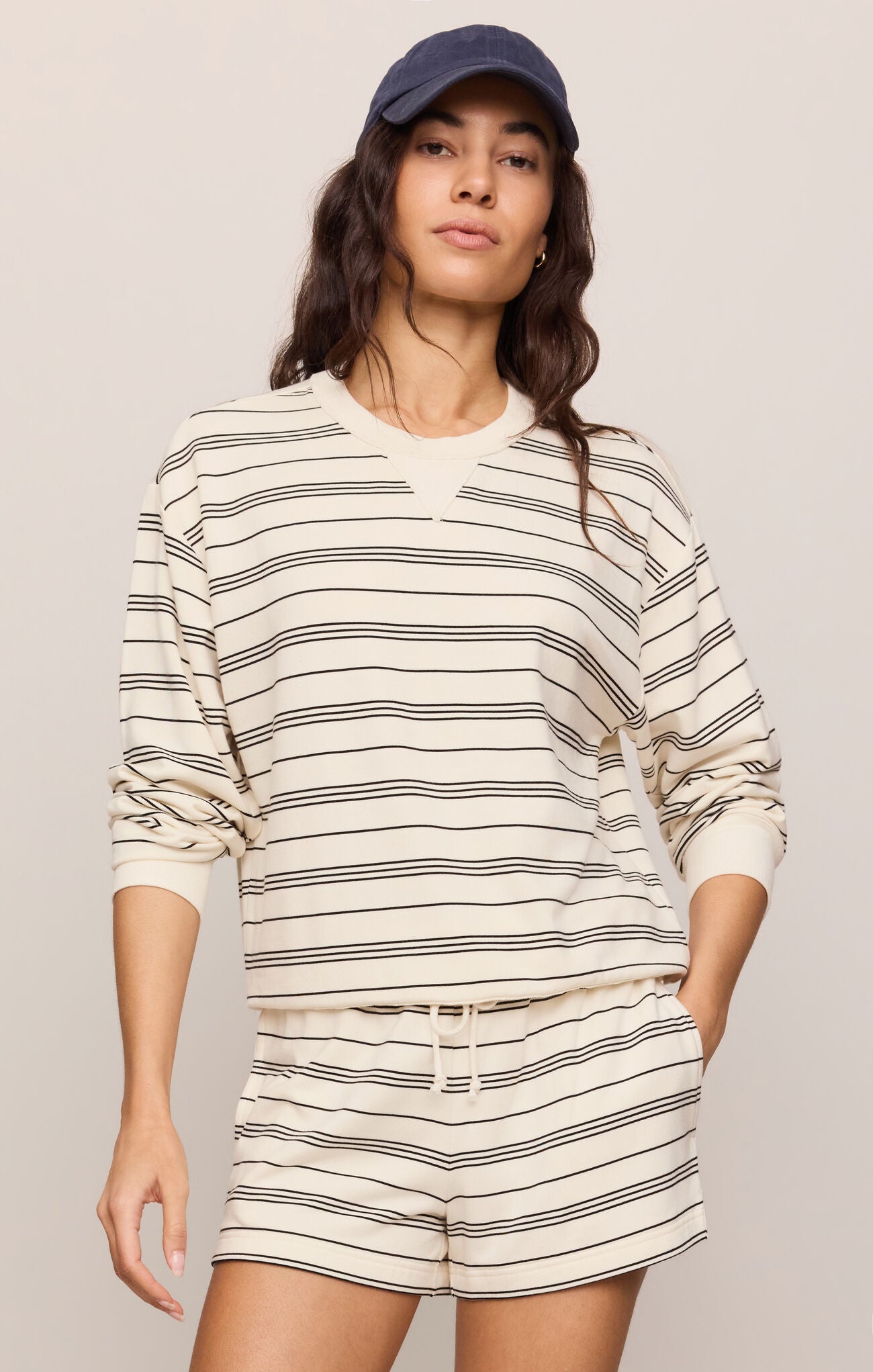 Woman wearing a striped long-sleeve top and shorts with a cap on a plain background