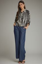 A chic zebra-print woven top featuring dramatic poncho sleeves, a classic shirt collar, button-front closure, and a feminine scalloped hem.