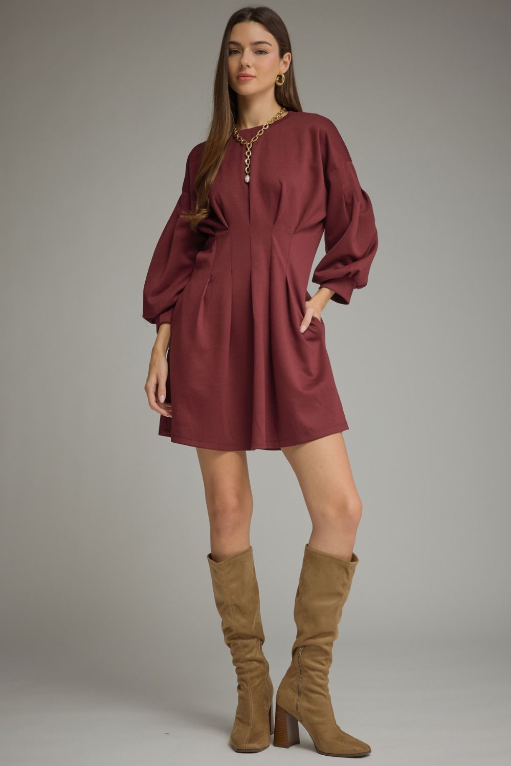 A timeless solid mini dress featuring a flattering pleated waist, classic round neckline, long sleeves, and convenient side pockets.

