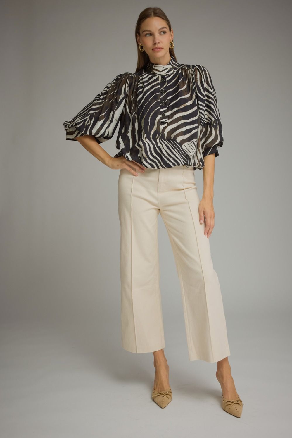 A statement-making zebra print top featuring elegant ¾ balloon sleeves, a stand collar, gathered details, and a polished banded hem.

