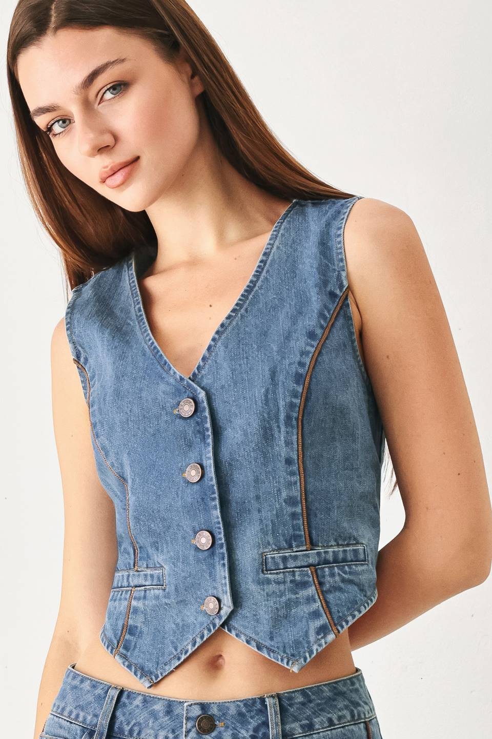 Model wearing the Winslet Washed Denim Vest featuring a washed cotton-blend denim finish, front button closure, tailored fit, and piping detail from Pieces & Peaches boutique.