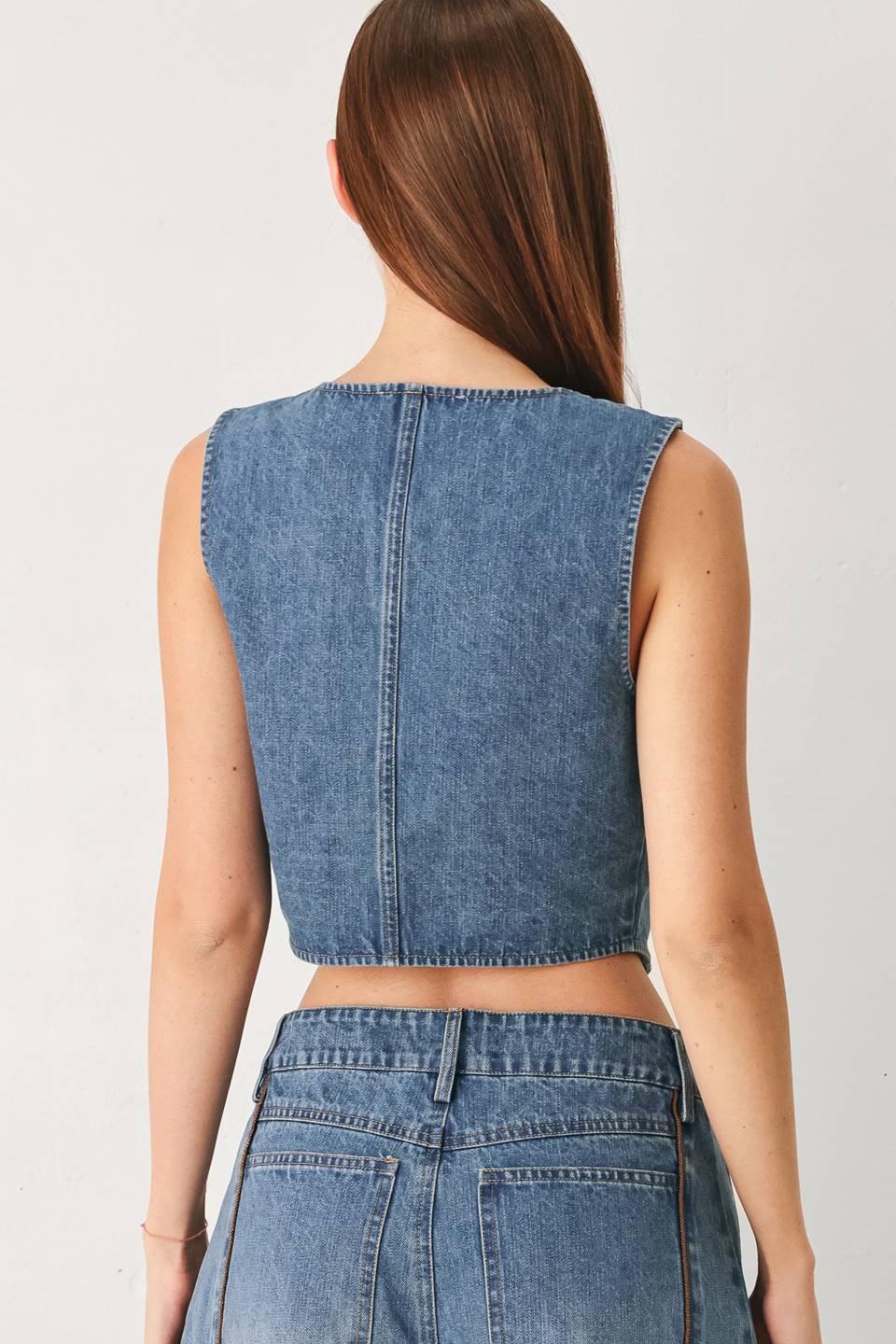 Model wearing the Winslet Washed Denim Vest featuring a washed cotton-blend denim finish, front button closure, tailored fit, and piping detail from Pieces & Peaches boutique.