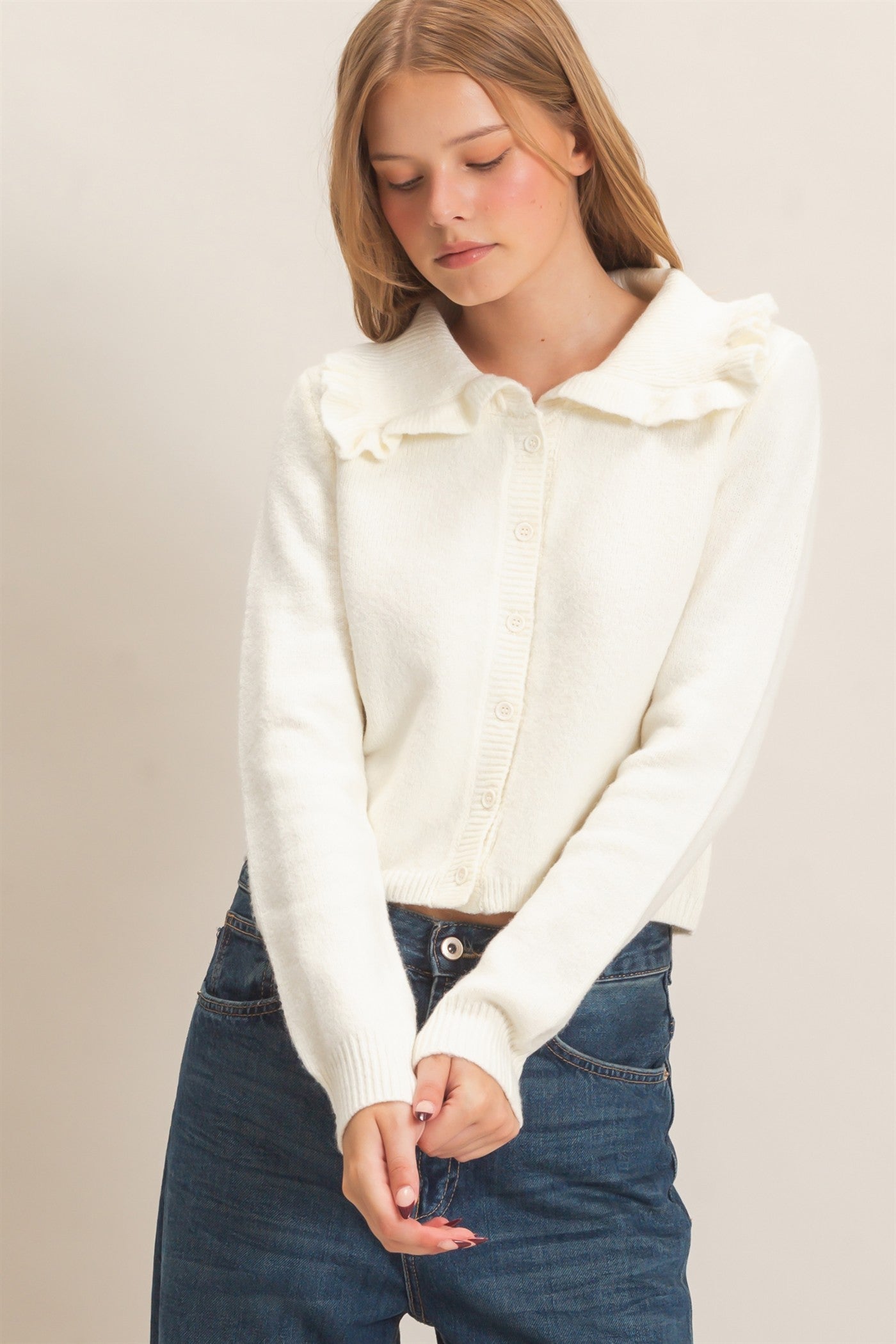 A polished knit cardigan featuring a feminine ruffled collar, classic button-front design, and ribbed cuffs for timeless everyday elegance.

