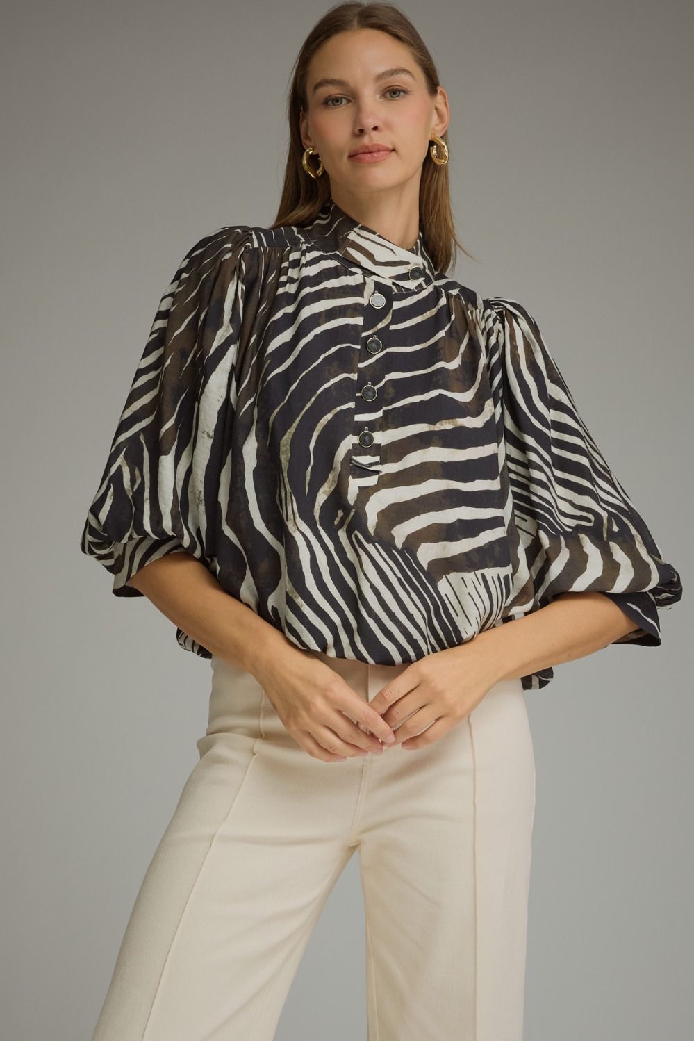 A statement-making zebra print top featuring elegant ¾ balloon sleeves, a stand collar, gathered details, and a polished banded hem.

