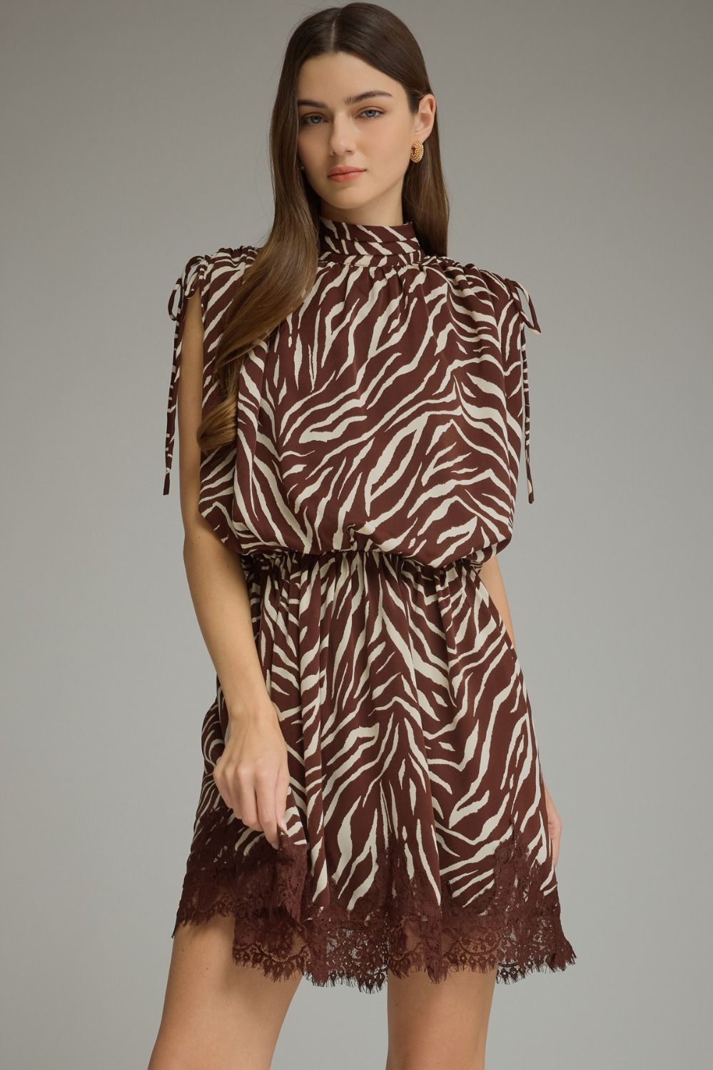 A statement-making zebra print mini dress featuring a mock neckline, self-tie shoulder details, elastic waist, and delicate lace-trimmed hem.

